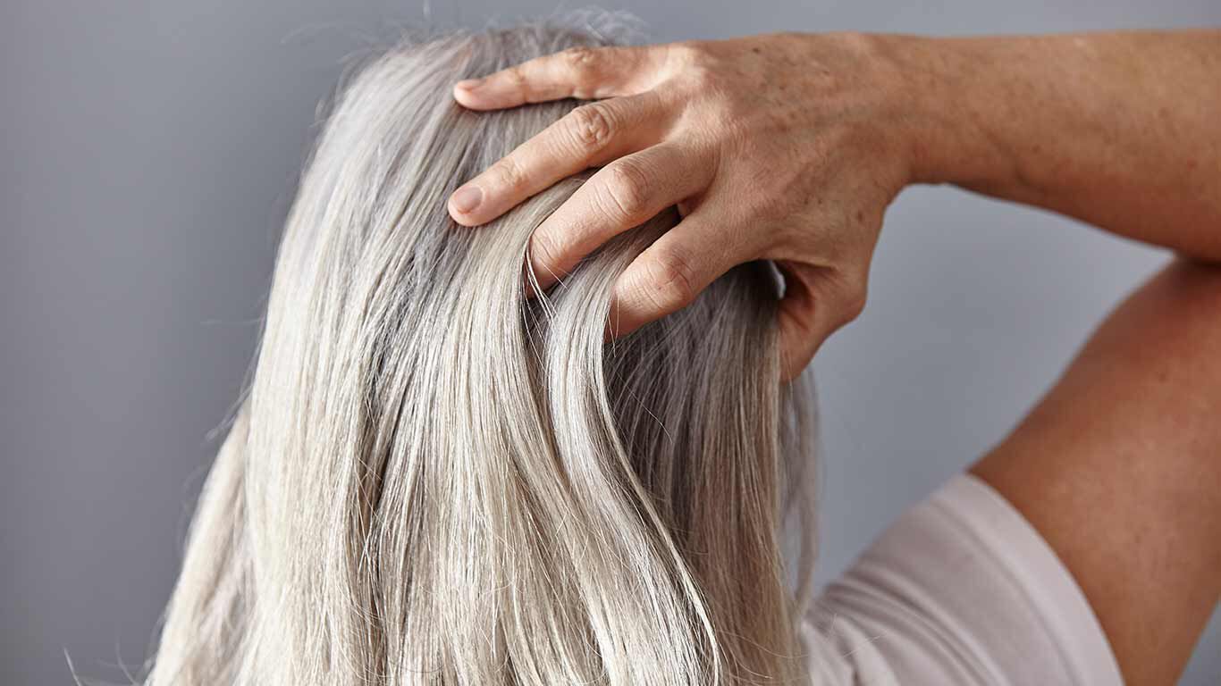 De vrouw raakt de achterkant van haar grijzende hoofd aan. 
